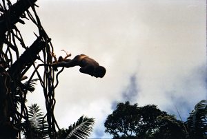 Rite of Passage showing an adolescent boy jumping from a high point toward the ground while his ankles are tied to rope and vines.
