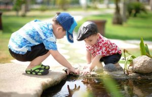 Two preschoolers crouched down by a small pond playing together