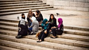 A group of young women, most are wearing a hijabi (head scarf), sitting on steps in a courtyard