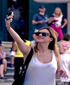 Young adult female holding up her cell phone to take a selfie.