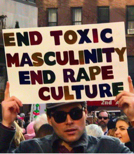 Young man in sunglasses is holding a sign above his head reading: "End Toxic masculinity. End rape culture."